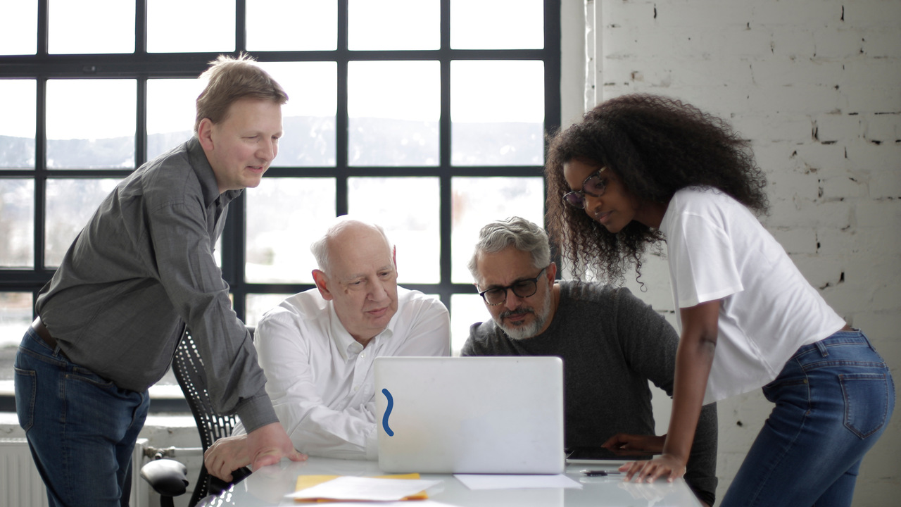 Equipe de 4 pessoas conversando em frente ao computador. Imagem simboliza o debate sobre ferramentas de gestão industrial.