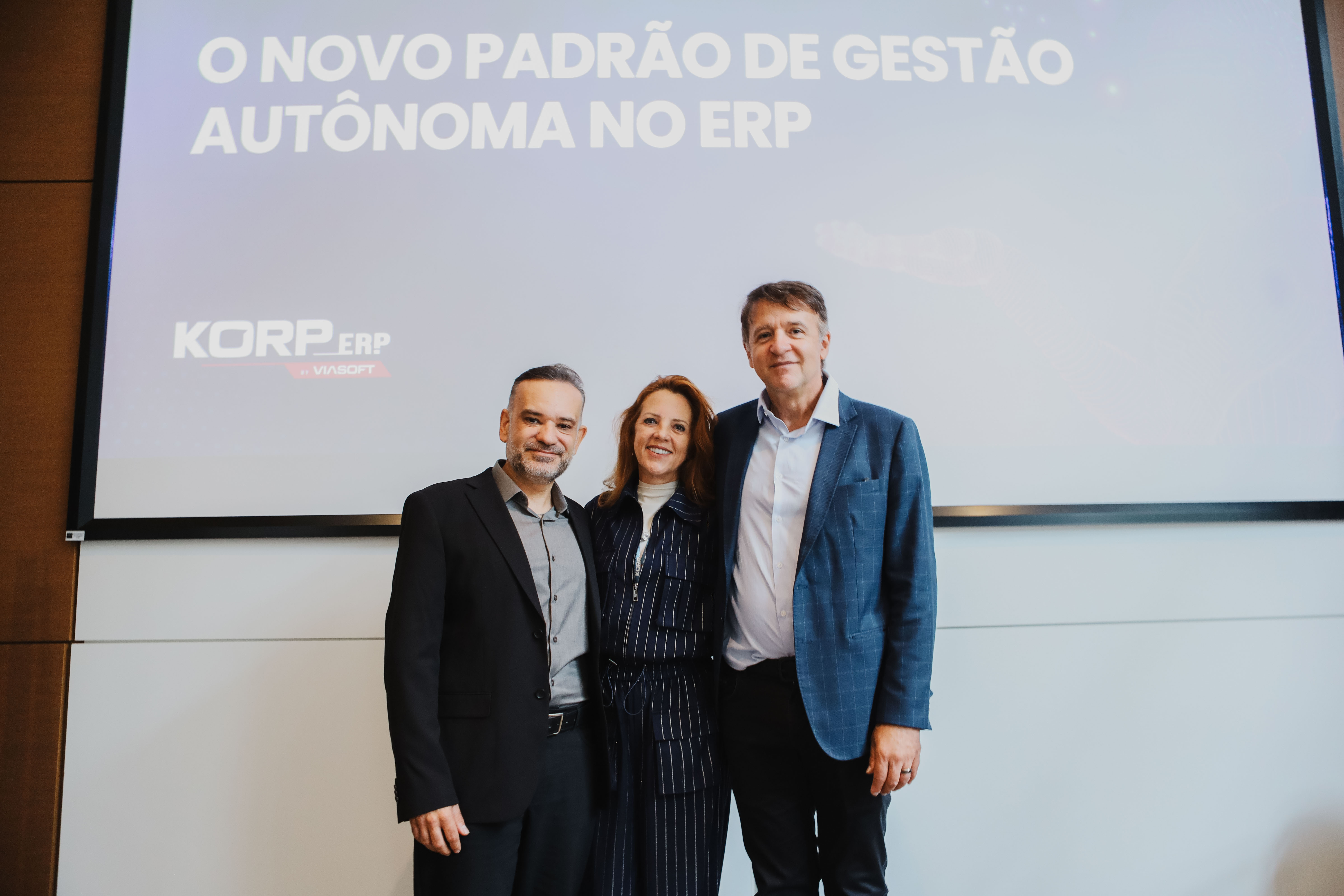 alexandre henzen, CEO, diretor de tecnologia e criador o brain, debora henzen, diretora administrativa e itamir viola, diretor comercial da korp abraçados em frente a um telão
